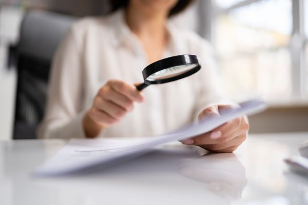 Person examining a document with a magnifying glass, illustrating analysis, verification and the legal value of evidence and data