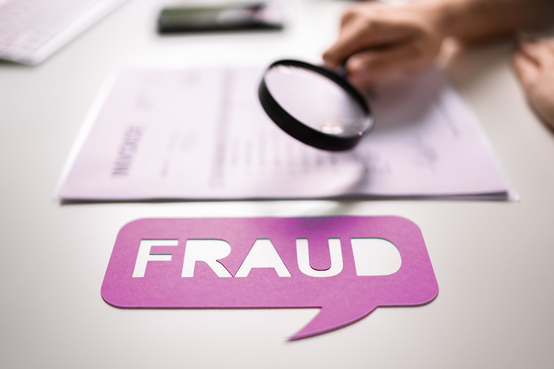 Loupe examinant un document avec le mot "fraud", illustrant la détection de fraude documentaire et la vérification de l’authenticité des documents