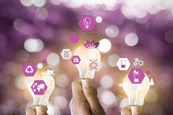 Main tenant des ampoules avec des icônes écologiques et énergétiques, illustrant l’innovation durable, les énergies renouvelables et la traçabilité énergétique